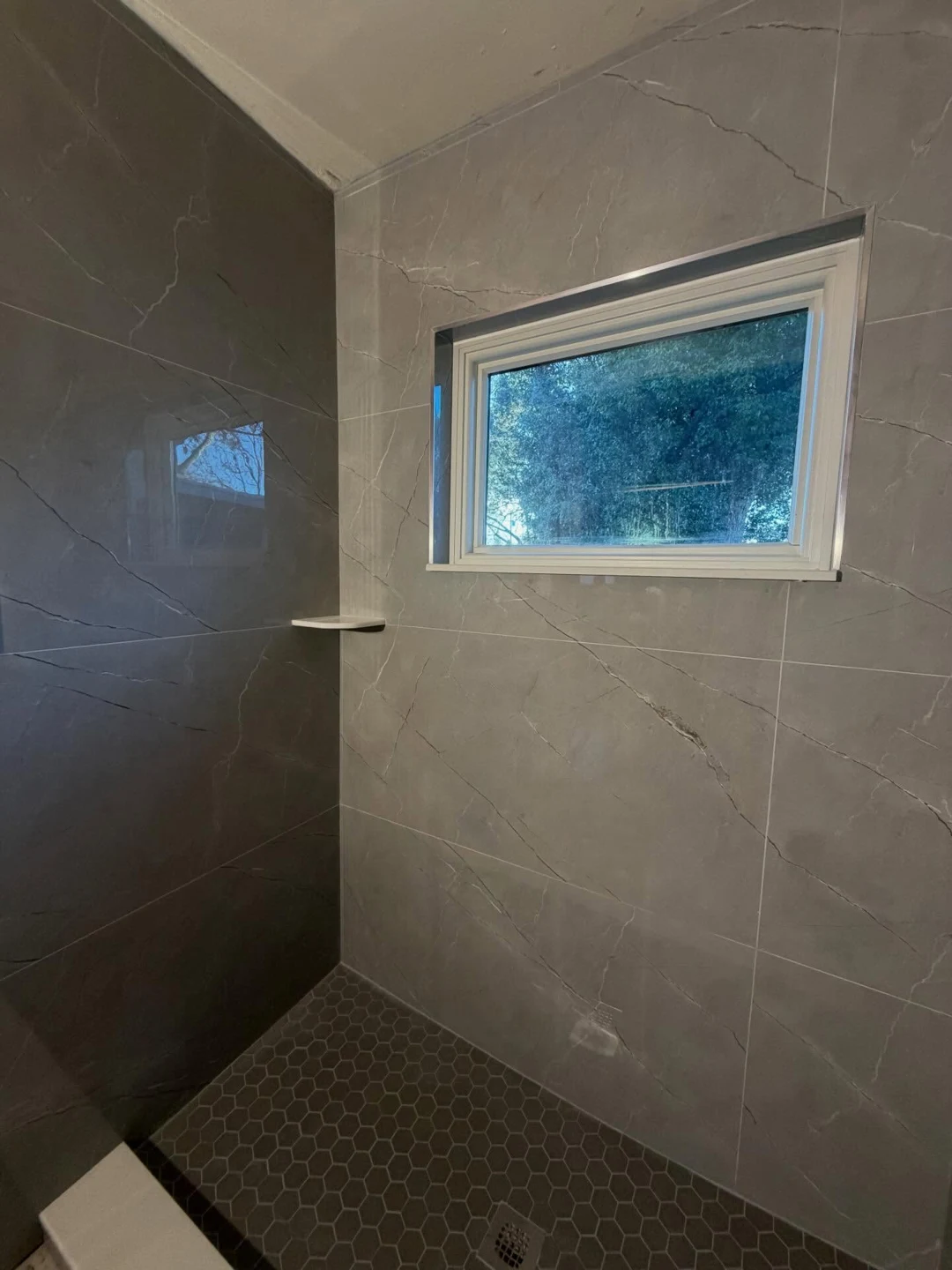 Renovated shower with gray tile and hexagonal floor